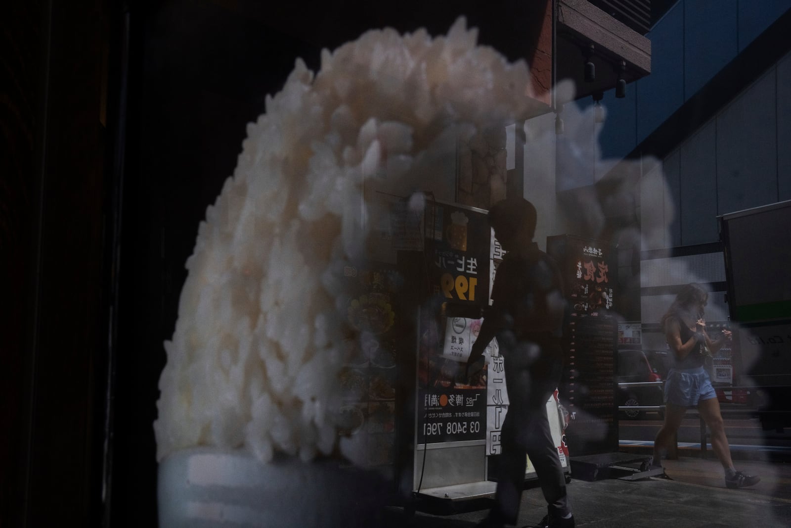 Pedestrians are reflected in the window of a restaurant advertising for rice in Tokyo, Thursday, May 22, 2025. (AP Photo/Louise Delmotte)
