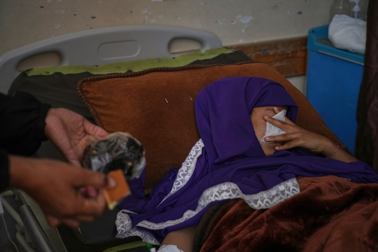 Asmaa Faraj, who was injured by shrapnel in an Israeli army strike, covers her face as her sister, Salwa, holds out cookies brought from home at Nasser Hospital in Khan Younis, Gaza Strip, Tuesday, May 6, 2025. (AP Photo/Abdel Kareem Hana)
