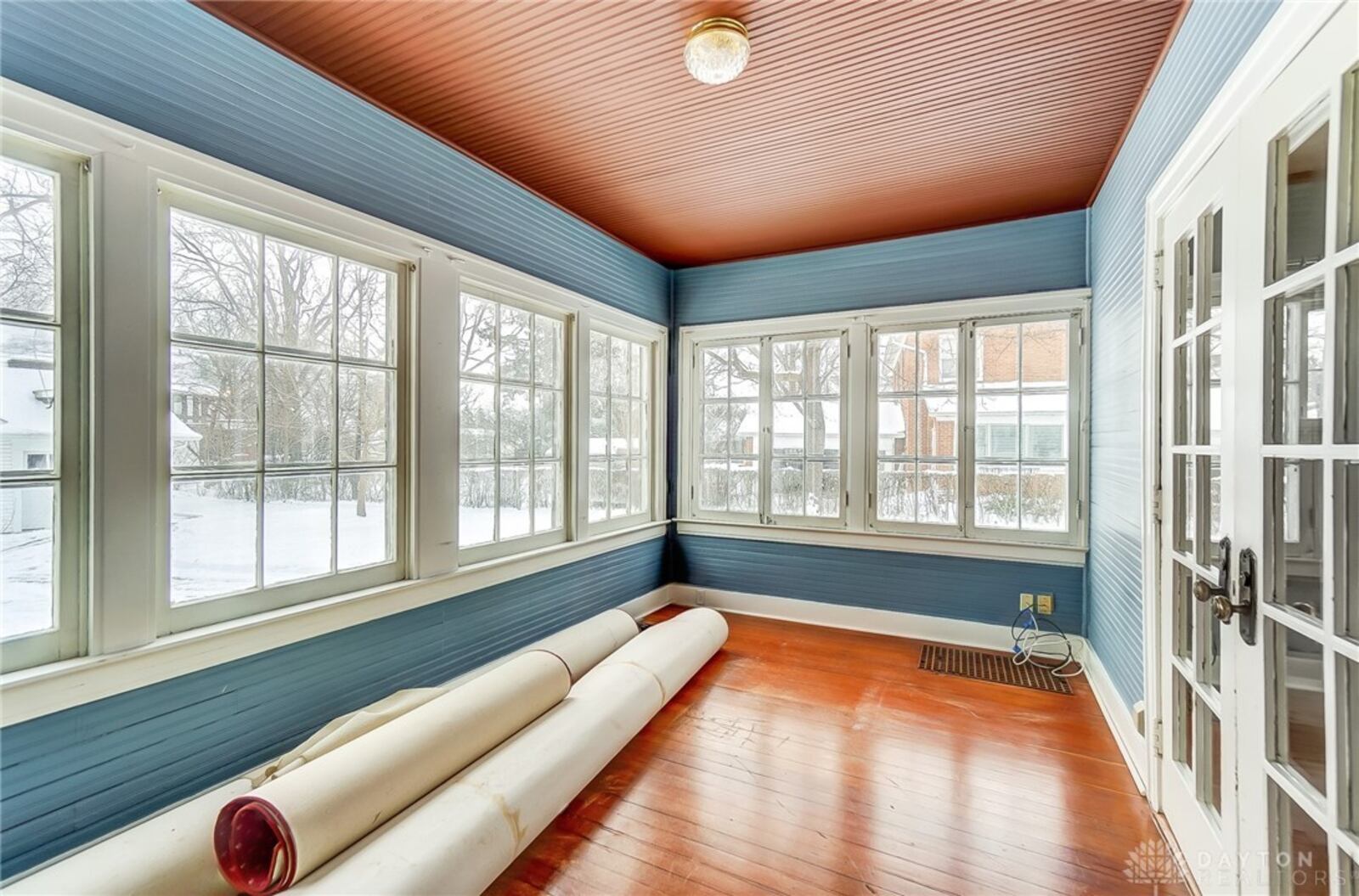 The sitting room is connected to the living room through French doors and has hardwood flooring and a beadboard ceiling.