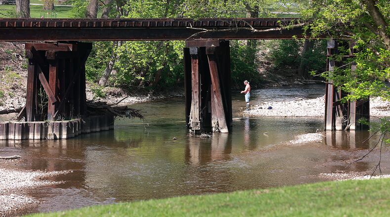 A man is seen through the railroad bridge over Buck Creek as he takes advantage of the warm sunshine Thursday, April 27, 2023 by doing some fishes off a sandbar in the middle of the creek at Snyder Park. Local tourism officials are promoting outdoor recreation, downtown public art tours and more in the new Greater Springfield Travel Guide. BILL LACKEY/STAFF