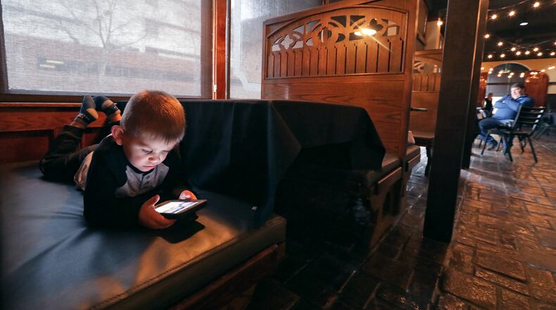 Callan Catanzaro, 3, plays on a phone Wednesday while his parents get their new restaurant, Fratelli's Famiglia Ristorante, ready for its grand opening. BILL LACKEY/STAFF
