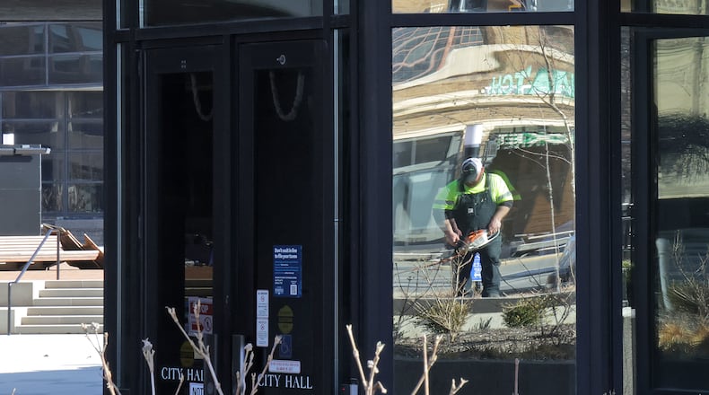 A City of Sprngfield Service Department worker is reflected in the mirrored windows of City Hall as he takes advantage of the warm weather and sunshine to clean up the landscaping around the building Friday, Feb. 28, 2025. BILL LACKEY/STAFF