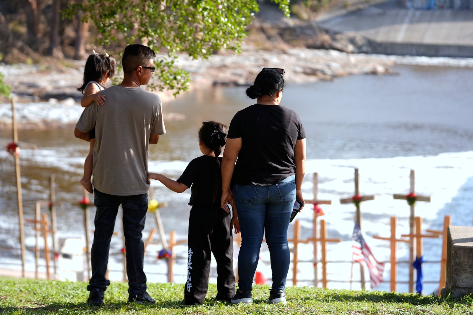 Kerrville residents Edgar Rojas, second from left, and his wife Perla, alongside daughters Emily, left, and Olivia, visit a memorial for flood victims along the Guadalupe River on Thursday, July 10, 2025, in Kerrville, Texas. (AP Photo/Gerald Herbert)