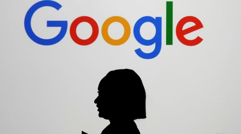 FILE - A woman walks by a giant screen with a logo at an event at the Paris Google Lab on the sidelines of the AI Action Summit in Paris, on Feb. 9, 2025. (AP Photo/Thibault Camus,File)