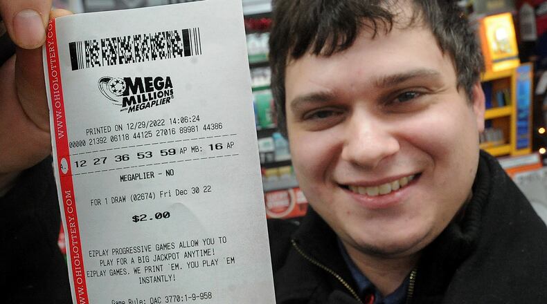 Travis Drew holds up his MEGA Millions ticket that he purchased Thursday Dec. 29, 2022 at Hall's Eastwood Market. MARSHALL GORBY\STAFF