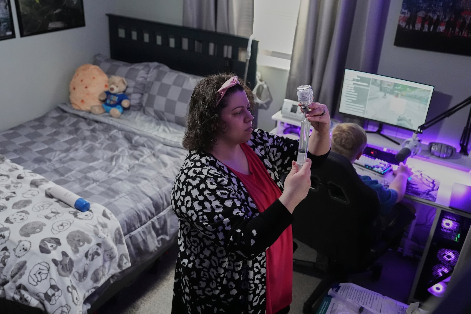 Jessica Blazier, center, prepares an infusion for her son, Julian, right, Wednesday, April 9, 2025, in Bloomfield, Ind. (AP Photo/Joshua A. Bickel)
