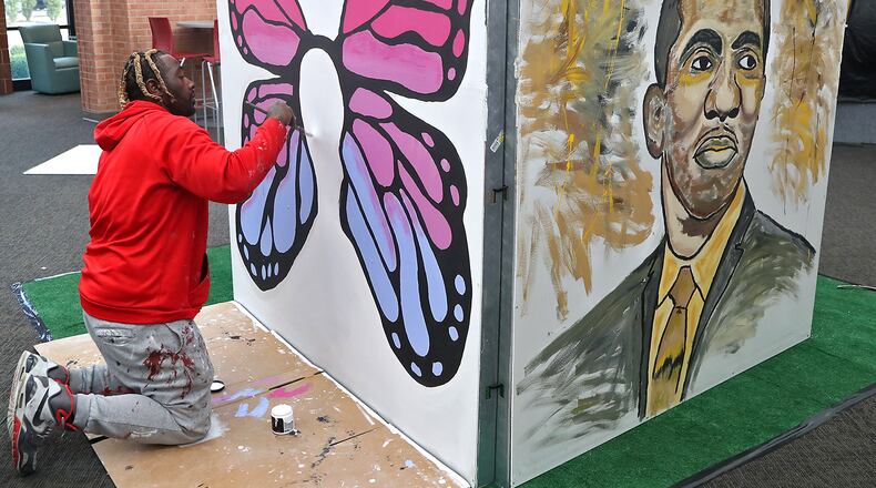 Byron Smith, from Dayton, paints a giant butterfly Wednesday, Oct. 19, 2022 as he helps set up for the Gem City Selfie Museum’s “Together We Rise!” Pop Up Exhibit in the Clark County Public Library's rotunda. The Gammon House and the Library are collaborating with a Dayton group on a unique interactive exhibition promoting mental health and community. The exhibit consists of four eight-foot by eight-foot panels with themes chosen specially relating to the Springfield community including one on the Gammon House, and one of Robert C. Henry, Springfield’s first Black mayor, pictured at right. BILL LACKEY/STAFF
