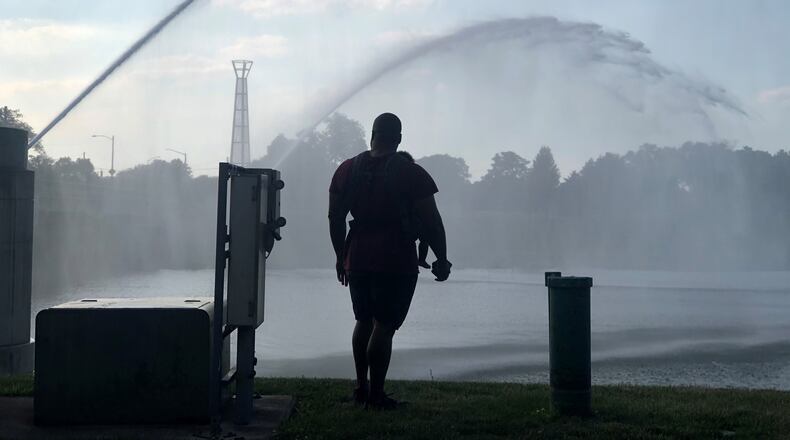 A man with a baby in a carrier watches the fountains in the river at RiverScape in the summer of 2020. CORNELIUS FROLIK / STAFF