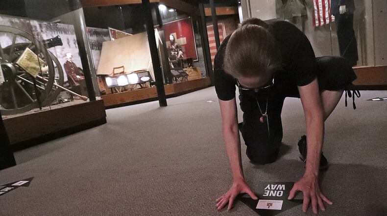Kasey Eichensehr presses down one of the direction arrows that the Clark County Heritage Center has put on the floors throughout the museum Thursday as they get ready for the opening of the museum next week. BILL LACKEY/STAFF