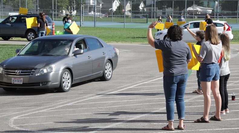 Global Impact STEM Academy teachers wave and greet the incoming students as they pick up their school supplies and computer Wednesday at a drive-thru at the school. GISA is starting school online for the first month and them will evaluate how things are going. BILL LACKEY/STAFF