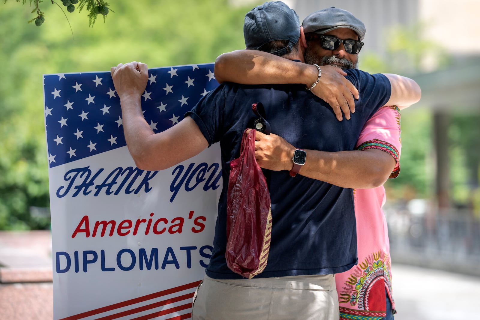 A man hugs former Foreign Service employee Bob Gilchrist, of Washington, left, as he holds a sign reading "Thank You America's Diplomats" outside the State Department headquarters, Friday, July 11, 2025, in Washington. (AP Photo/Mark Schiefelbein).