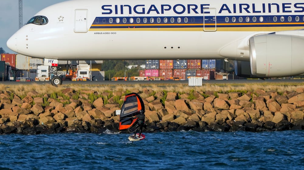 FILE - A man wing foils on Botany Bay as a Singapore Airlines passenger jet taxis after landing at Sydney Airport in Australia, Sept. 5, 2022. (AP Photo/Mark Baker, File)