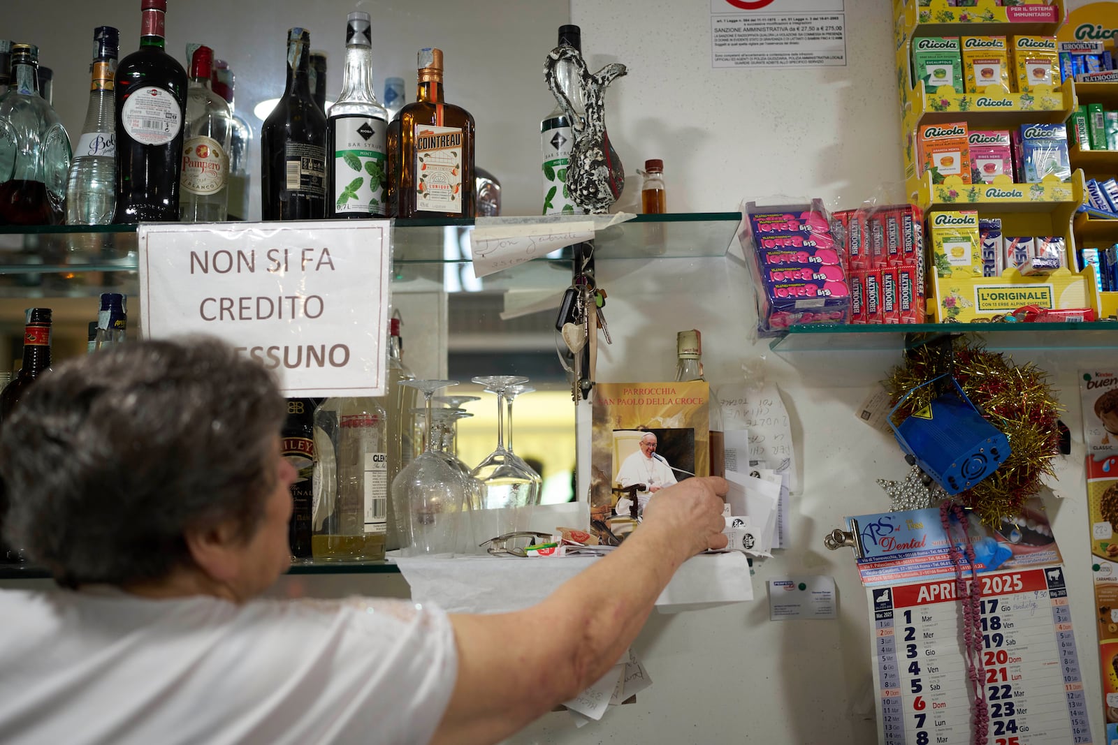 A woman adjusts a photo of the late Pope Francis in cafe in front of San Paolo Della Croce parish church in Corviale neighbourhood, in Rome, Sunday, May 4, 2025. (AP Photo/Alessandra Tarantino)
