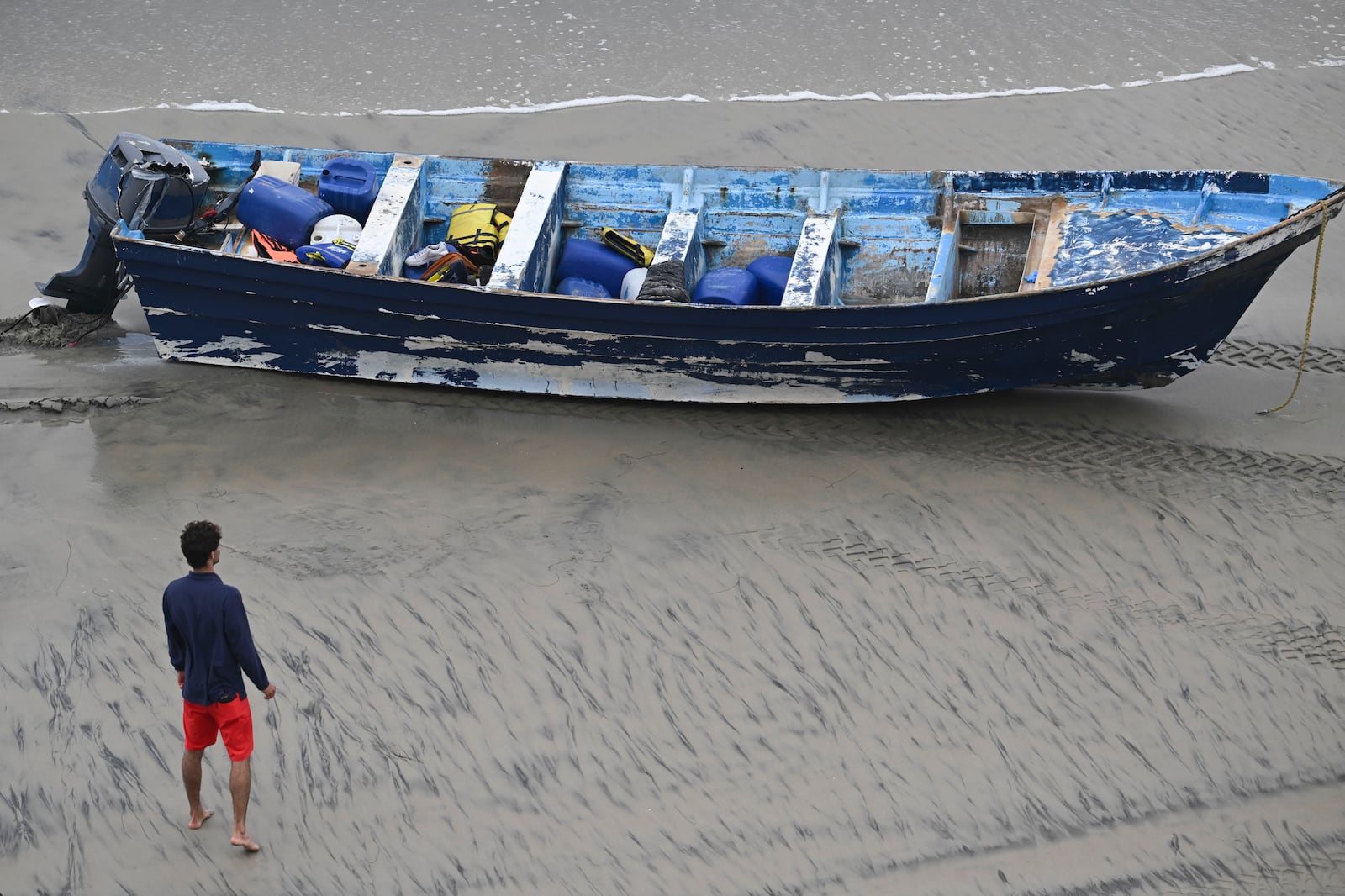 A Del Mar lifeguard looks over a capsized boat on the beach Friday, May. 5, 2025, in at Torrey Pines State beach in San Diego, Calif. (AP Photo/Denis Poroy)