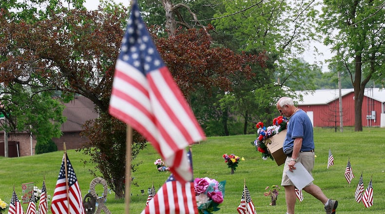 Don Lee, from Netts Floral Company and Greenhouse, carries a box full of red, white and blue flower arrangements Wednesday, May 24, 2023 as he walks through the sea of Amarican flags at Rose Hill Burial Park looking for the graves to place the flowers on.  BILL LACKEY/STAFF