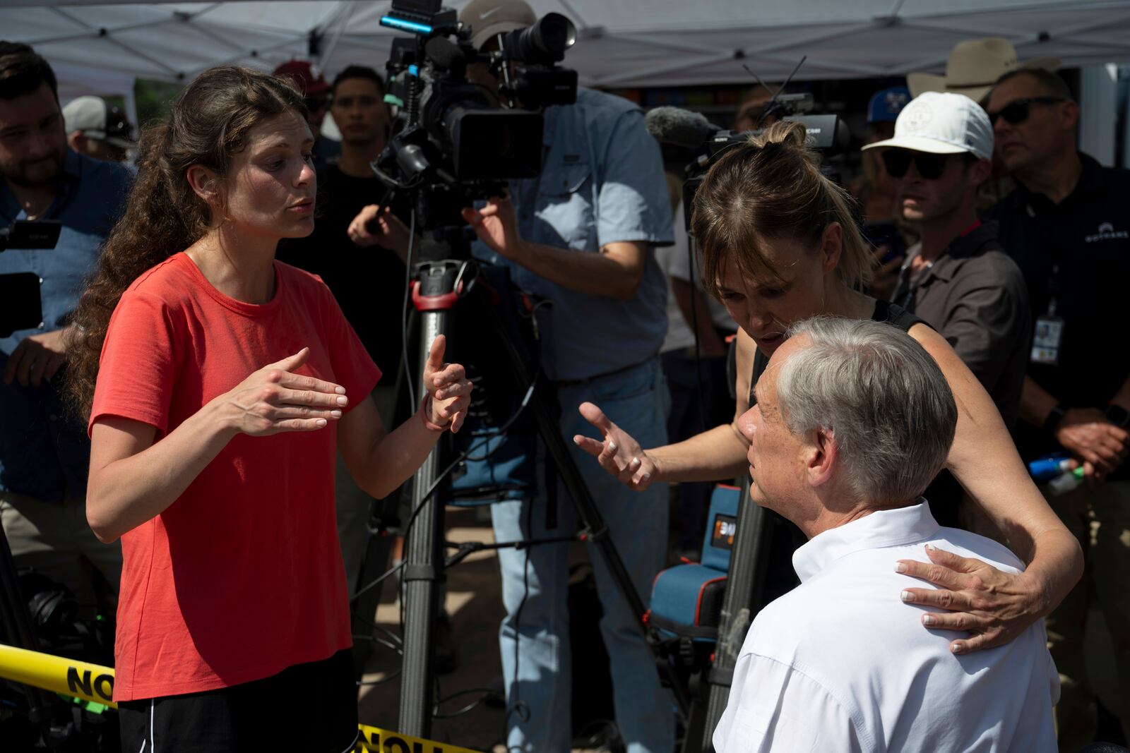 Courtney Calhoun, a resident in Kerr County, left, and Renee DeRese, top right, confront Texas Gov. Greg Abbott on Tuesday, July 8, 2025, in Hunt, Texas. (AP Photo/Eli Hartman)