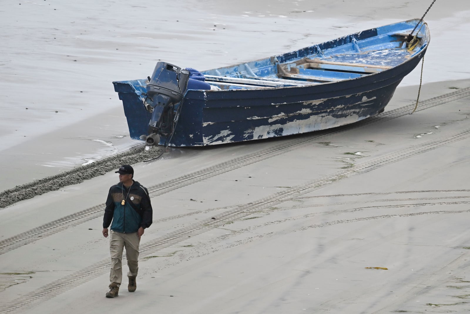 A law enforcement officer walks past capsized boat on the beach Monday, May 5, 2025, in at Torrey Pines State beach in San Diego, Calif. (AP Photo/Denis Poroy)