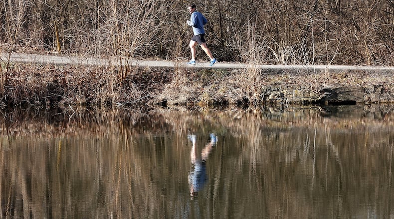 A man is reflected in the water at Hosterman Lake as he takes advantage of the sunshine in this March 1, 2023, photo as he runs through George Rogers Clark Park. BILL LACKEY/STAFF