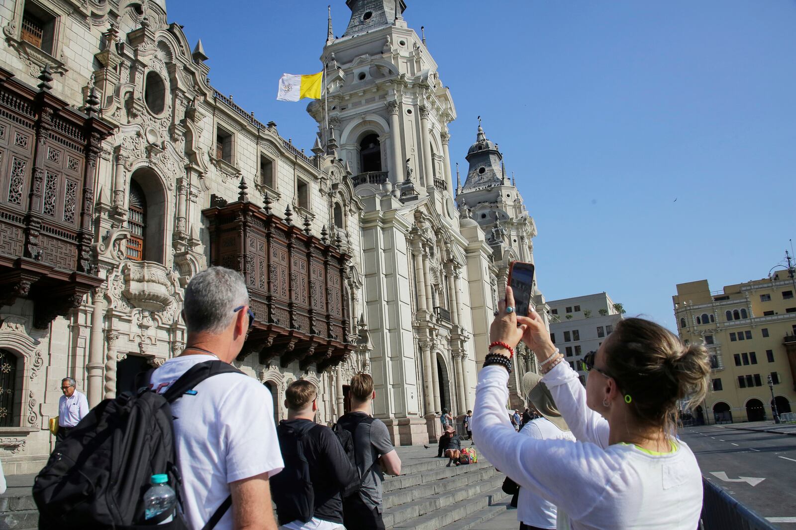 A woman photographs the Vatican flag flying above the Cathedral in Lima, Peru, following the election of Robert Prevost, a dual citizen of the United States and Peru who served as a missionary and bishop in the country, as Pope Leo XIV, Thursday, May 8, 2025. (AP Photo/Cesar Zamalloa)