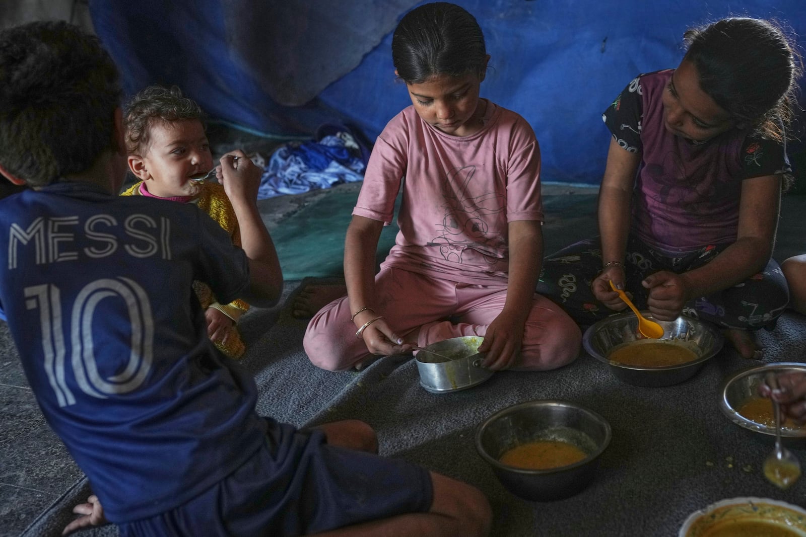 Children from the Saqr family eat lentil soup cooked by their mother at their family tent in Gaza City, Saturday, May 24, 2025. (AP Photo/Jehad Alshrafi)