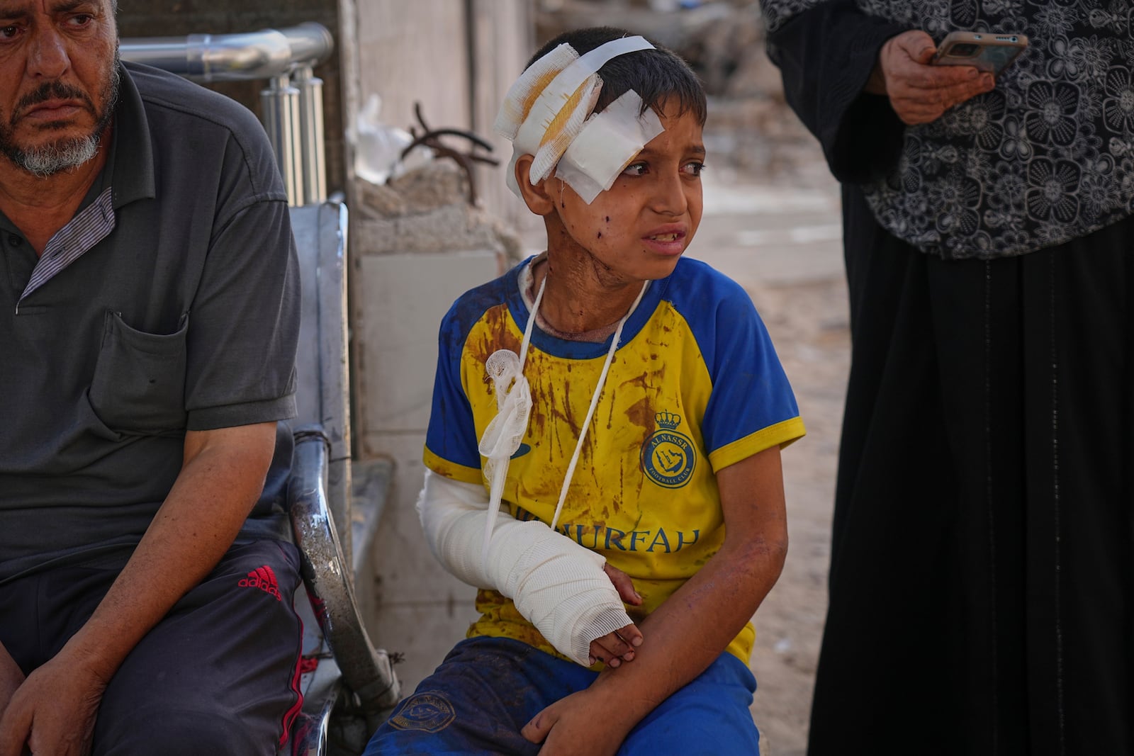 Hamam Al-Farani, sits along with other family members as the body of his father, Alaa, killed in an Israeli army strike that also injured the boy, is prepared for burial at Shifa hospital in Gaza City, Tuesday, June 24, 2025. (AP Photo/Jehad Alshrafi)