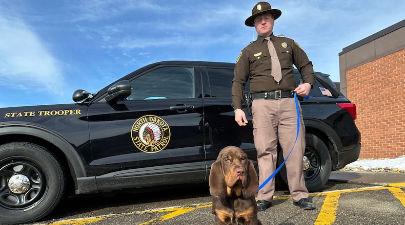 North Dakota Highway Patrol Trooper Dustin Pattengale and Beau, a bloodhound puppy, pose for a photo on Friday, Feb. 27, 2026, outside the Highway Patrol office in Fargo, N.D. (AP Photo/Jack Dura)