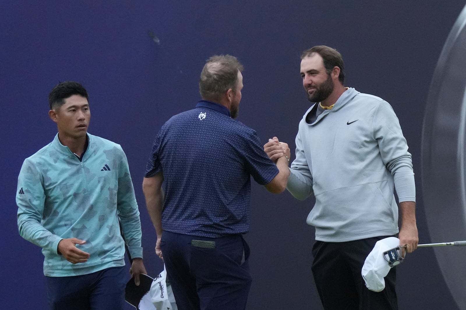 Scottie Scheffler of the United States, right, shakes hands with Shane Lowry of Ireland,center and Collin Morikawa of the United States looks on, as they complete their second round of the British Open golf championship, on the 18th green, at the Royal Portrush Golf Club, Northern Ireland, Friday, July 18, 2025. (AP Photo/Jon Super)
