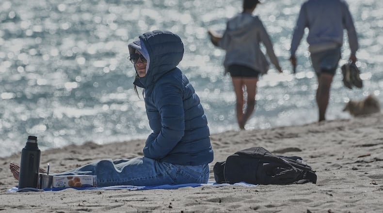 A bundled up Lucia Amato, of Argentina, sits on the shore while waiting for a friend in Miami Beach, Fla., Thursday, Jan. 29, 2026.A bundled up (AP Photo/Marta Lavandier)