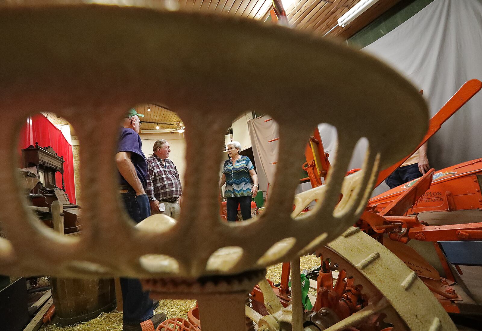 Bob Wood, left, his wife, Sharon,  and Dan Hearlihy are seen through metal seat on the antique Champion Reaper they had just delivered to Hearlihy at his museum Tuesday. BILL LACKEY/STAFF