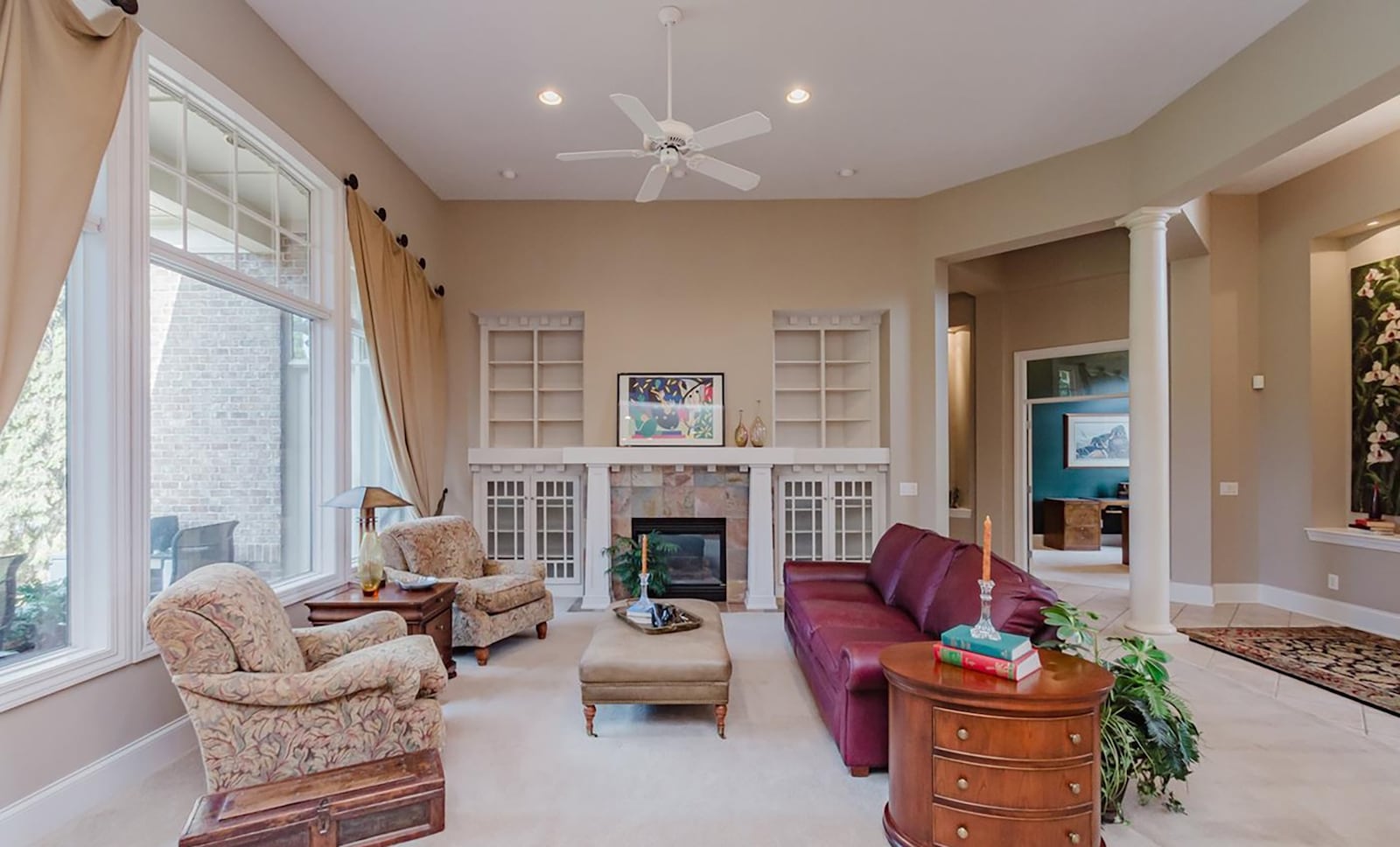 The living room has a two story ceiling, ceiling fan, built in bookcases on either side of a gas fireplace and a wall of windows. CONTRIBUTED