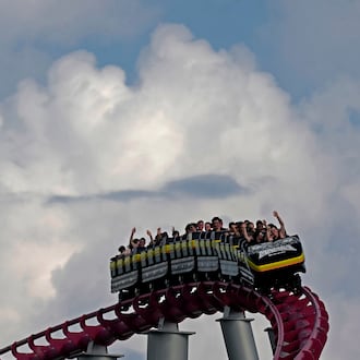 People ride on the Mamba roller coaster at Worlds of Fun theme park as storm clouds build in the distance on the first full day of summer Friday, June 21, 2024, in Kansas City, Mo. (AP Photo/Charlie Riedel)