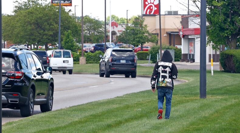 A pedestrian walks through the grass along Bechtle Avenue Friday, May 10, 2024. Springfield officials have approved funding for construction of sidewalks along the busy central commercial and business area of Bechtle Avenue. BILL LACKEY/STAFF