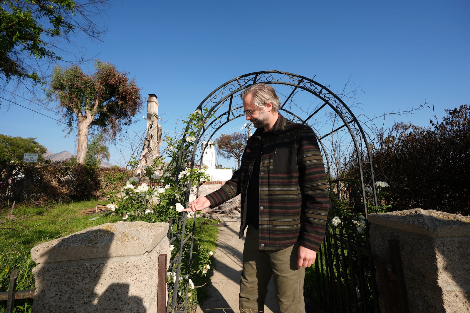 Tim Vordtriede holds white roses at the gate of his property, which was destroyed the Eaton Fire in Altadena, Calif., on Tuesday, April 22, 2025. (AP Photo/Damian Dovarganes)