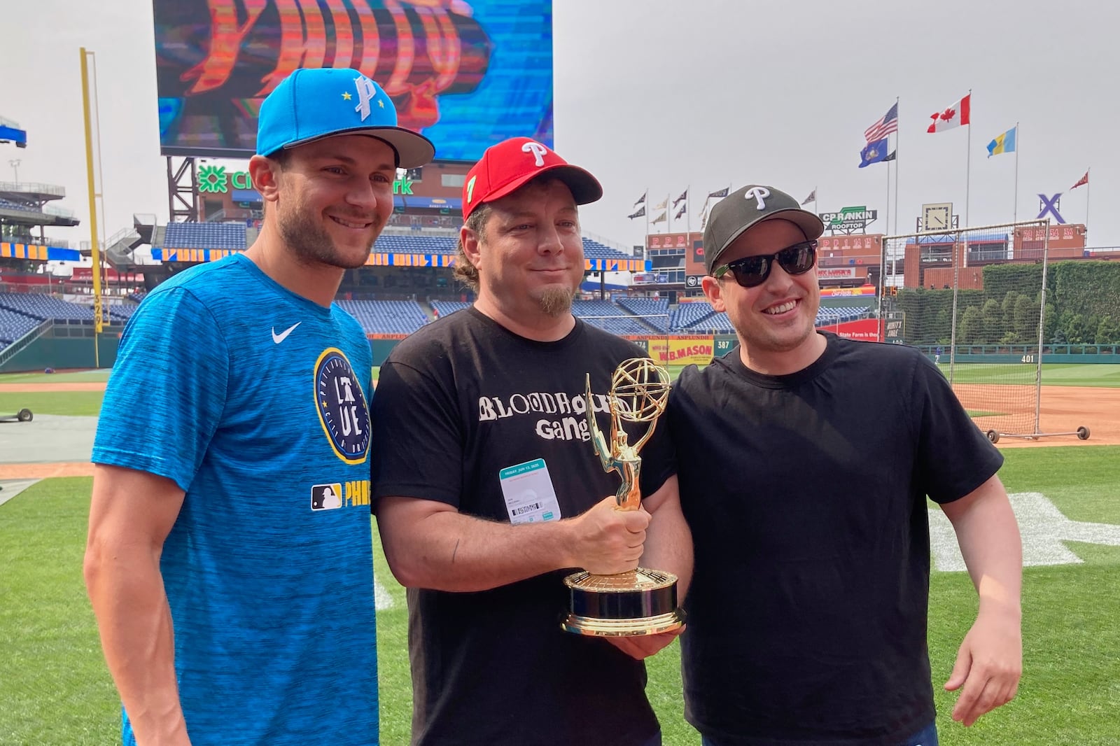 Philadelphia Phillies shortstop Trea Turner, left, poses with Phillies fan Jon McCann, center, and documentary producer Kyle Thrash with a sports Emmy won for best sports documentary "The Turnaround", the story how McCann inspired a city-wide movement to cheer for instead of boo for Turner, before a baseball game against the Toronto Blue, Jays, Friday, June 13 , 2025, in Philadelphia (AP Photo/Dan Gelston)