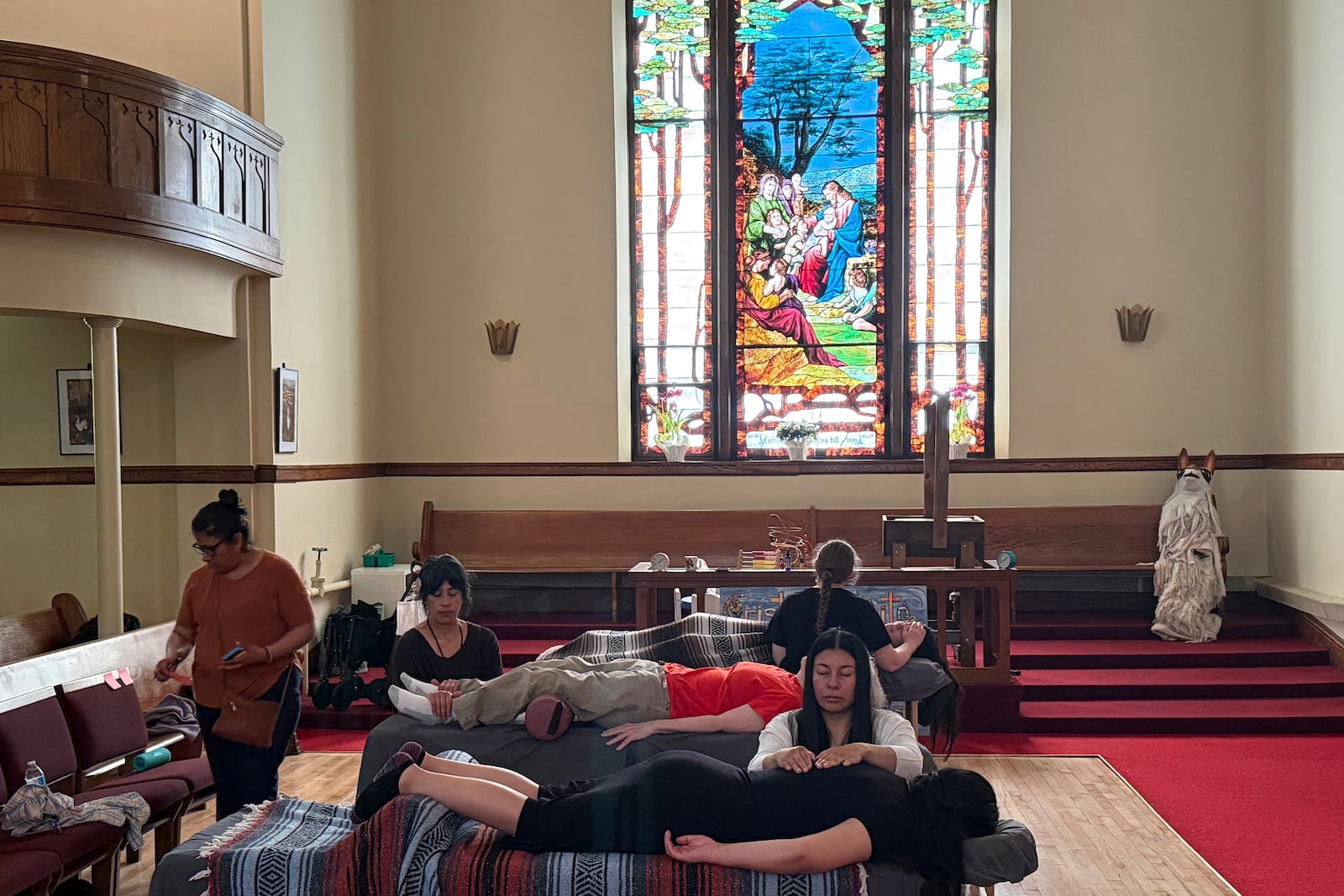 Guadalupe Gonzalez, foreground center, and two other practitioners perform Reiki treatments in the sanctuary of St. Paul’s-San Pablo Lutheran Church, where congregant Lizete Vega, left, helped organize wellness sessions as part of its migrant ministry, in Minneapolis, Sunday, April 27, 2025. (AP Photo/Giovanna Dell’Orto)