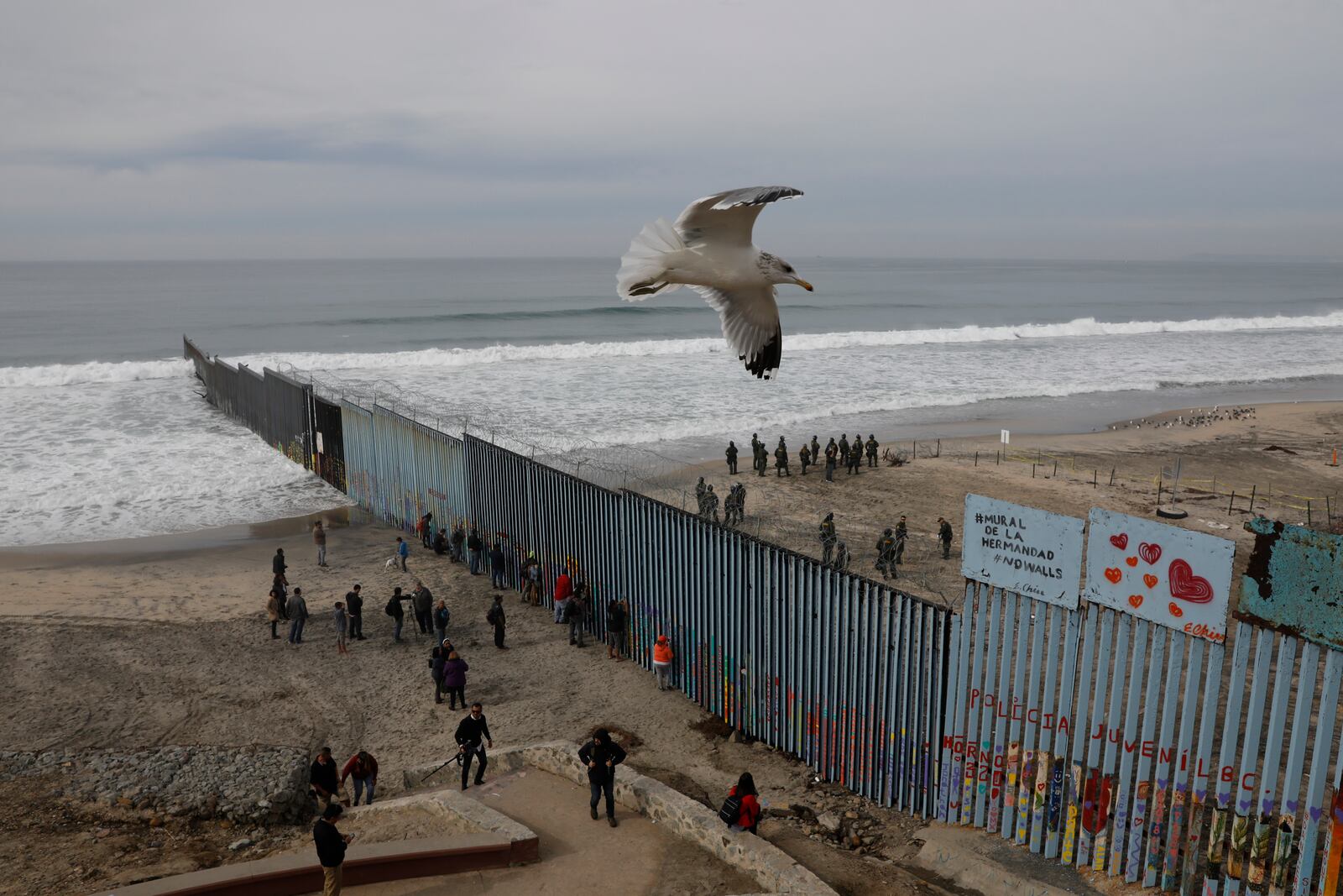 FILE - People peer through the border wall as U.S. Border Patrol in San Diego prepare for the arrival of hundreds of pro-migration protesters, in Tijuana, Mexico, Dec. 10, 2018. (AP Photo/Rebecca Blackwell, File)