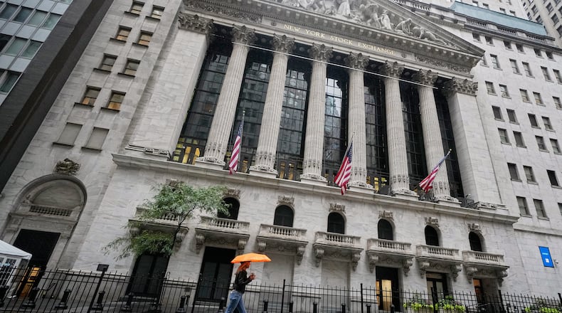 A woman with an umbrella passes the New York Stock Exchange, Monday, Oct. 13, 2025. (AP Photo/Richard Drew)