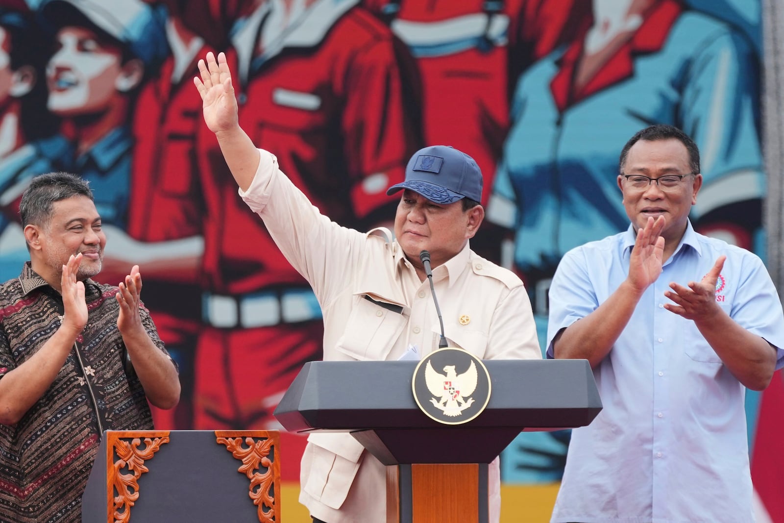 Indonesian President Prabowo Subianto, center, waves at the crowd as labor group leaders Said Iqbal, left, and Jumhur Hidayat, right, applaud during a May Day rally at the National Monument in Jakarta, Indonesia, Thursday, May 1, 2025. (AP Photo/Tatan Syuflana)