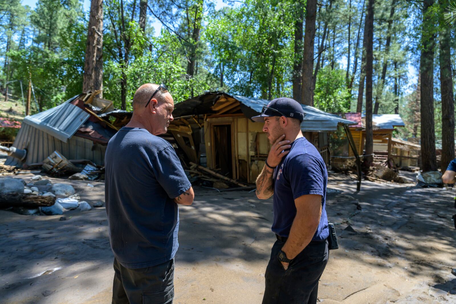 Ruidoso Fire Department member Price Bowen, right, speaks with resident Dan Privett as they stand on what would still be Dan's front porch, Wednesday morning, July 9, 2025, in Ruidoso, N.M., after flash floods yesterday swept away properties and RV's along the Rio Ruidoso. (AP Photo/Roberto E. Rosales)