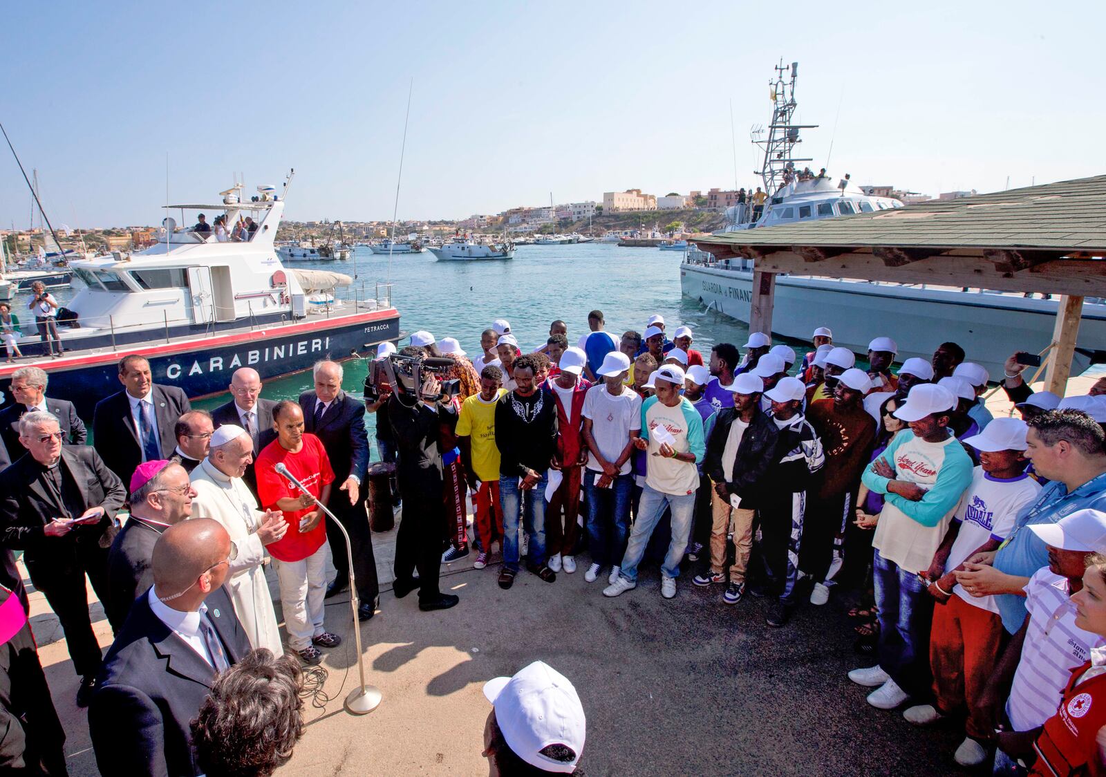 FILE-- Pope Francis, left, speaks to migrants, wearing white caps, during his visit to the island of Lampedusa, Sicily, in southern Italy, July 8, 2013. (AP Photo/Alessandra Tarantino, Pool, File)