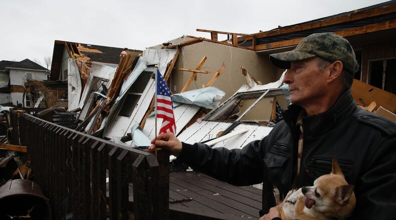 Ron Watt picks up a small flag he found in the rubble of his house and places it on what’s left of his porch Friday morning in Lakeview. BILL LACKEY/STAFF