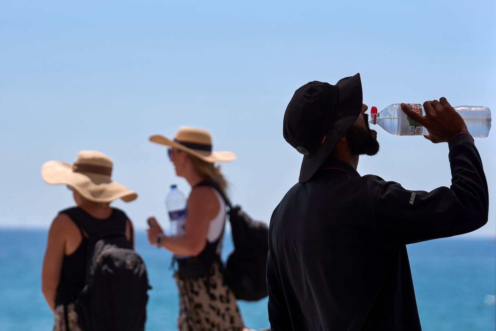 FILE - A tourist drinks water on a hot day at the beach in Barcelona, Spain, July 2, 2025. (AP Photo/Emilio Morenatti, File)