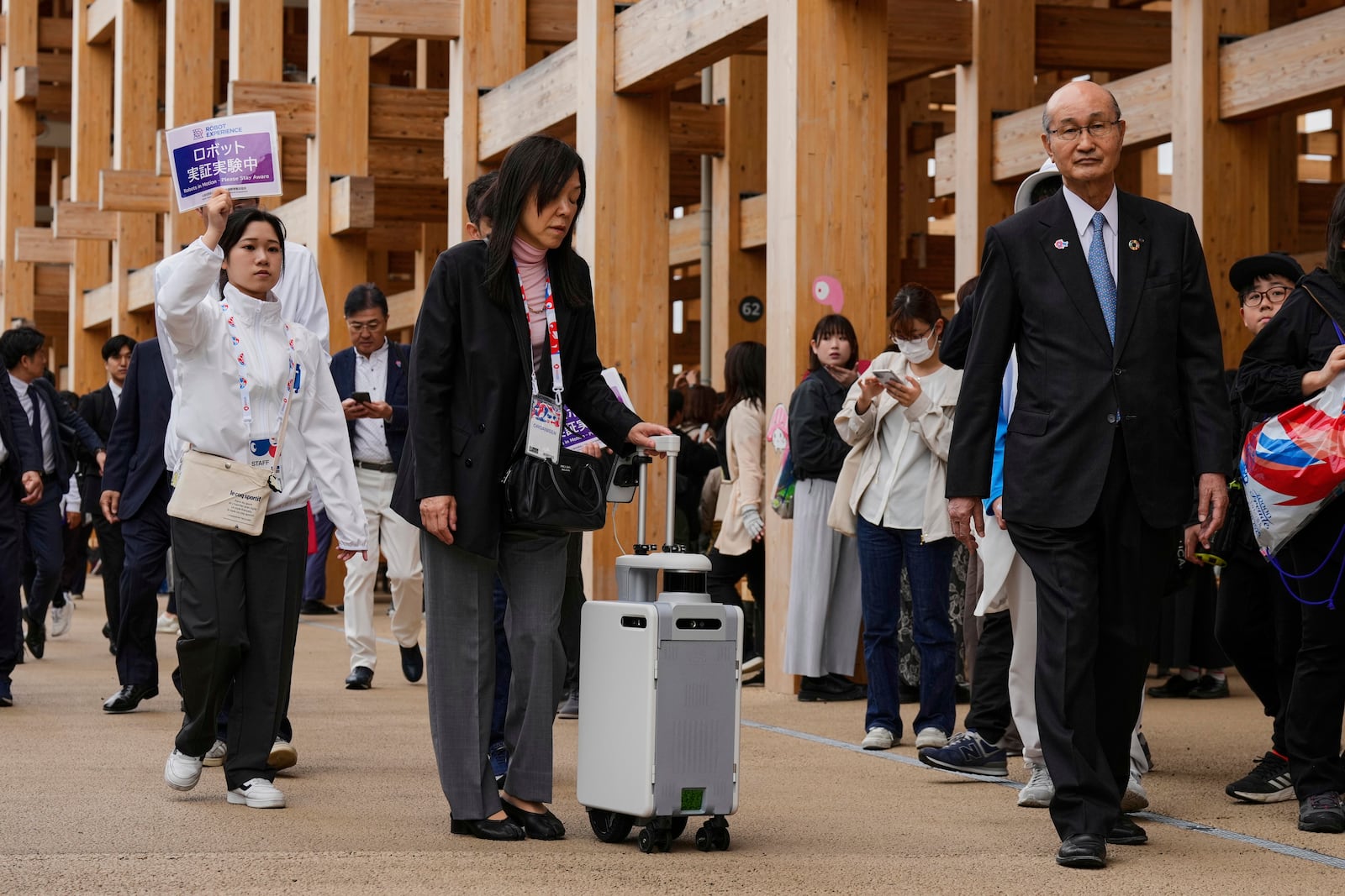 An organizer, center, uses a robot to help navigate those who have visual Impairment, as they show its testing at the Expo 2025 on the opening day in Osaka, central Japan, Sunday, April 13, 2025. (AP Photo/Hiro Komae)