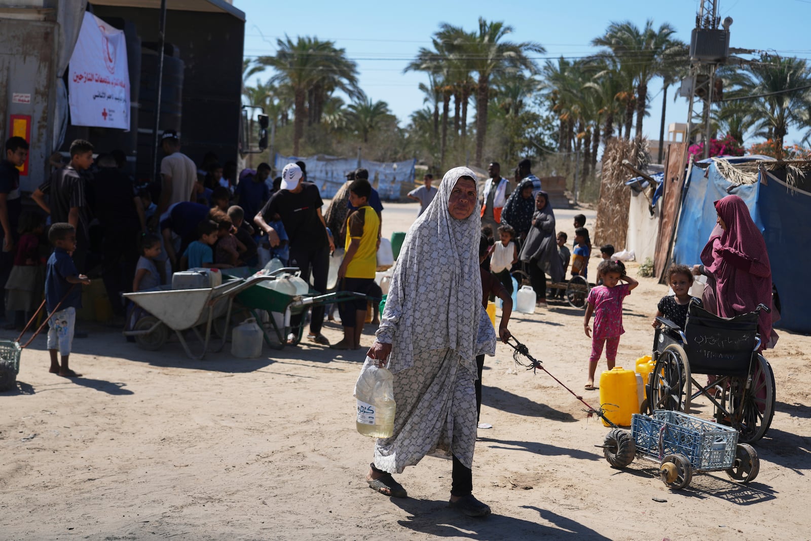 A Palestinian woman carries a container of water at a camp for the displaced in Deir al-Balah, Gaza Strip, Monday, July 7, 2025. (AP Photo/Abdel Kareem Hana)