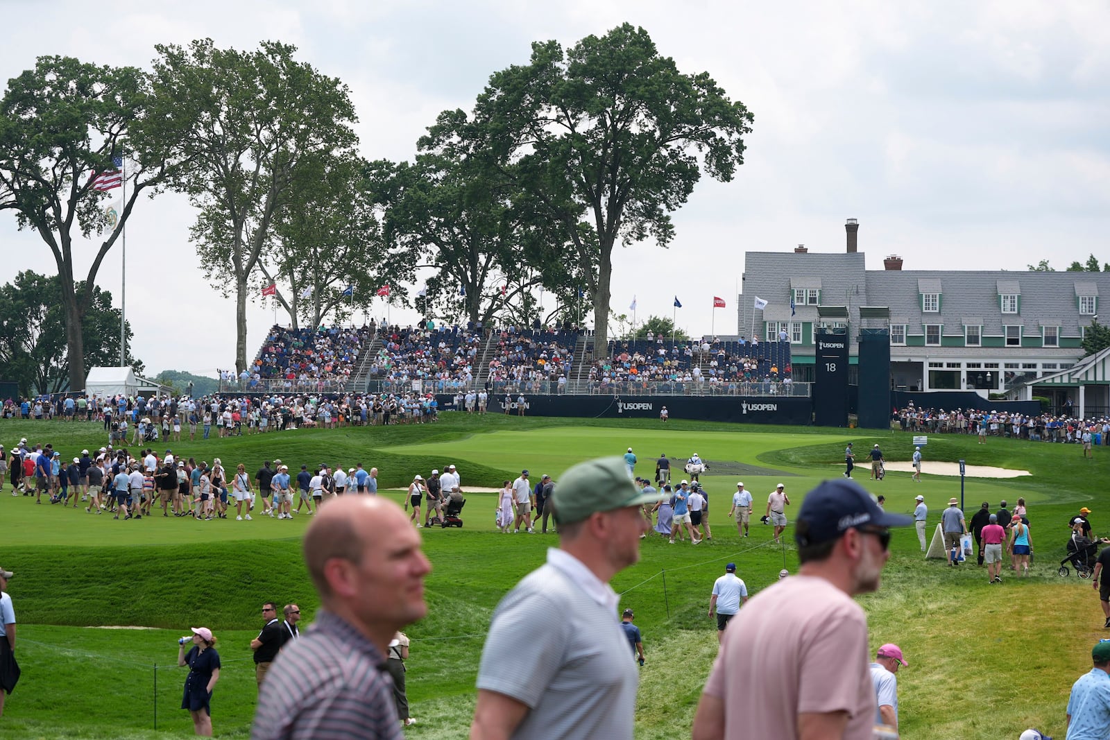 Fans cross the 18th fairway, in front of the green and clubhouse, between groups of golfers during a practice round for the 2025 US Open golf championship at Oakmont Country Club in Oakmont, Pa., Monday, June 9, 2025. (AP Photo/Gene J. Puskar)