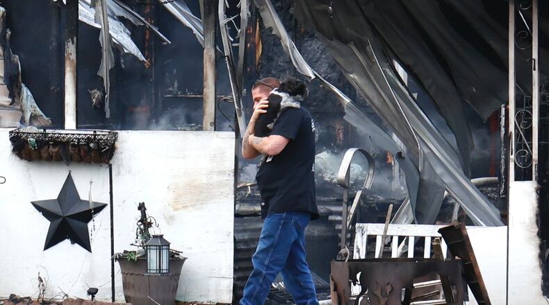 The owner of a mobile home surveys the damage fire caused to his trailer as he carries one of his two dogs that were rescued Tuesday, Nov. 29, 2022 along South Tecumseh Road. BILL LACKEY/STAFF
