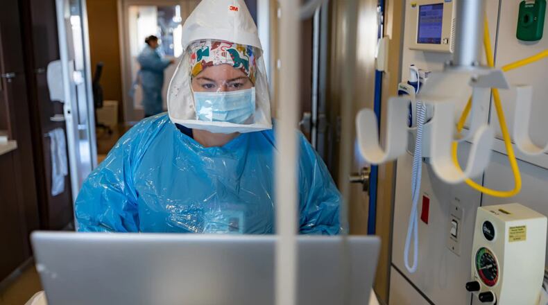 Taylor Spicer is a nurse at Miami Valley Hospital nurse. She is wearing full personal protective equipment, including an oxygen tank on her back, as she enters data for a COVID-19 patient in the hospital's COVID-19 unit.