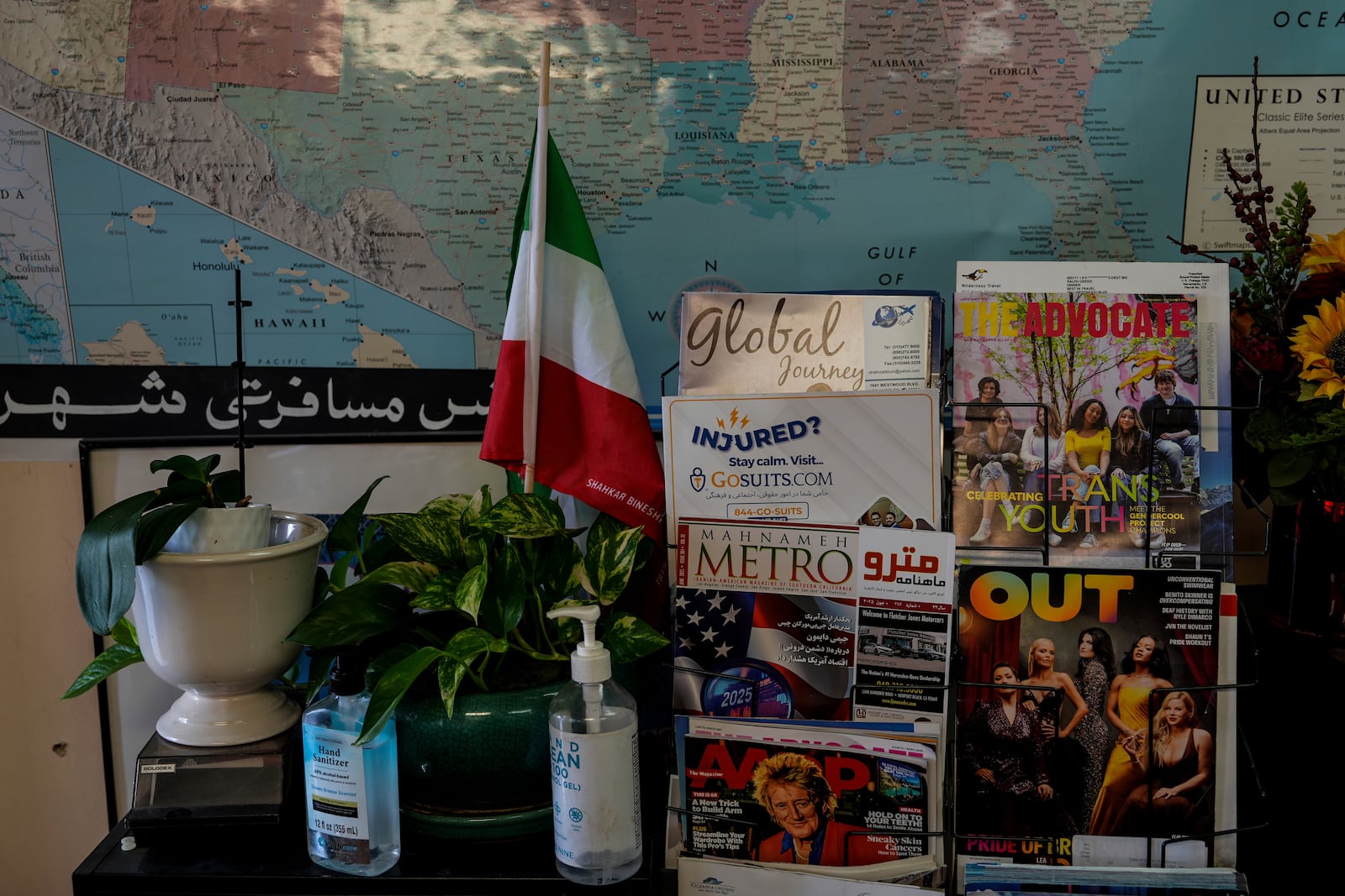 An Iranian flag is seen next to a magazine rack at Shahrzad Tahouri's travel agency in the "Tehrangeles" neighborhood of Los Angeles Tuesday, June 24, 2025. (AP Photo/Jae C. Hong)