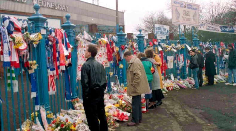 FILE- In this file photo dated April 17, 1989, soccer fans arrive to pay their respects and look at the flowers, scarves and banners, left on the gates at Hillsborough Football Stadium. (AP Photo/ Peter Kemp, File)