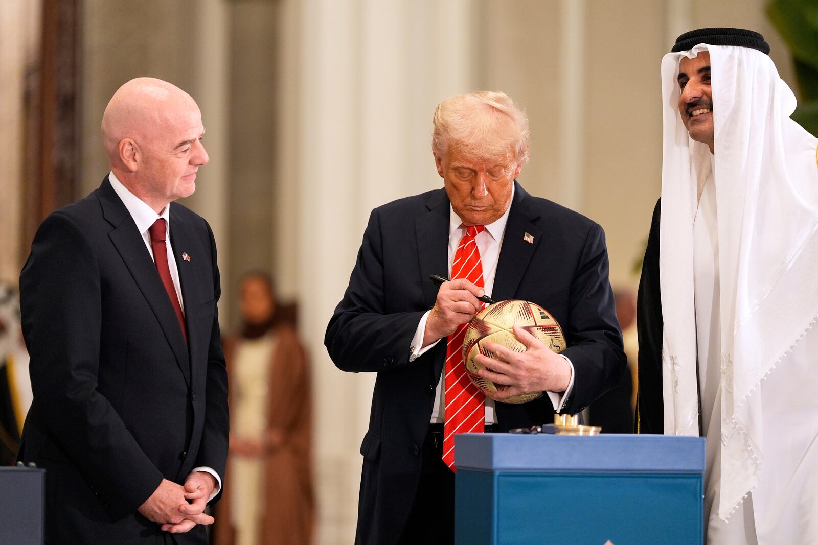 President Donald Trump signs a FIFA soccer ball as Qatar's Emir Sheikh Tamim bin Hamad Al Thani and FIFA President Gianni Infantino looks on at the Lusail Palace, Wednesday, May 14, 2025, in Doha, Qatar. (AP Photo/Alex Brandon)